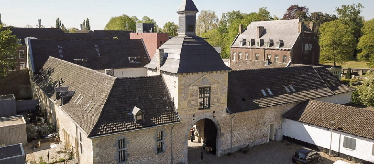 Historisch poortgebouw met binnenplaats en omliggende monumentale gebouwen in groene omgeving.
