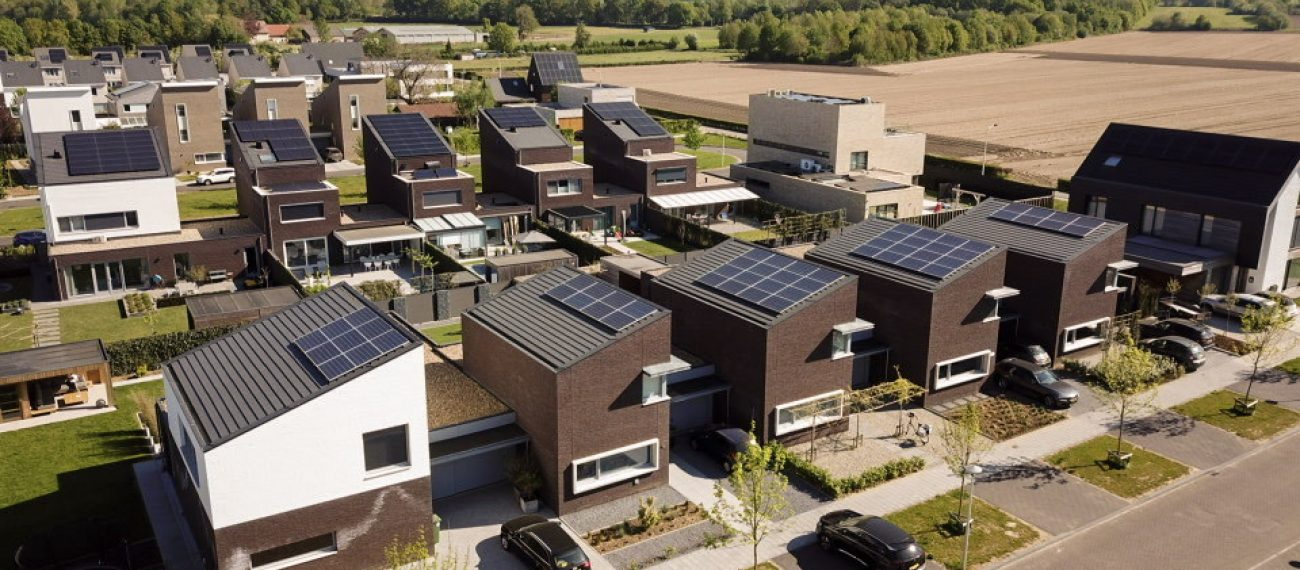Luchtfoto van moderne woningen met zonnepanelen op de daken in een nieuwbouwwijk met omliggende velden.