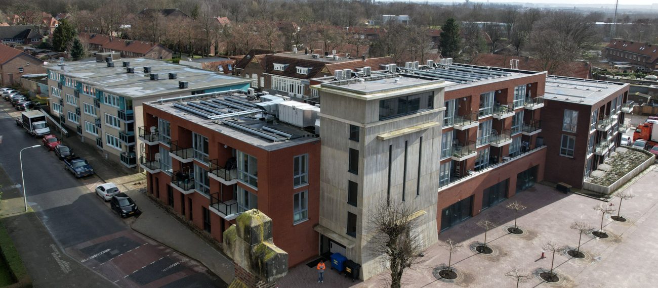 MFA Hart voor Treebeek Brunssum – luchtfoto van bakstenen complex met betonnen toren, balkons en plat dak met installaties aan plein met bomen