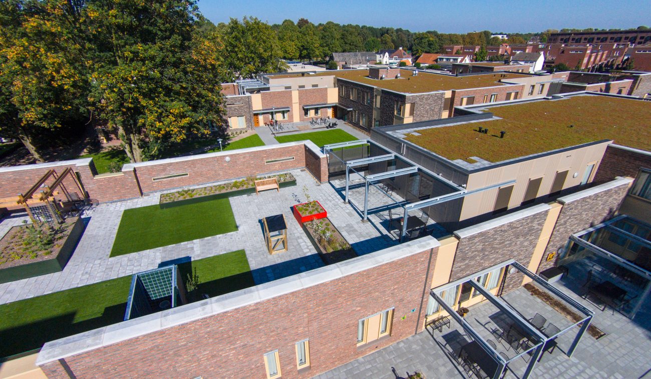 Hof verpleeghuis Venray, sierbestrating met grasvakken, zitbanken en baksteengevels.