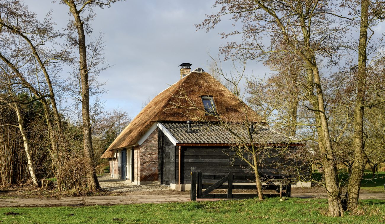Gerestaureerde woonboerderij Naardermeer: rieten kap, zwart houten bijgebouw, bomen en erfpad