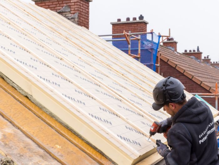 Vakman met schroefmachine monteert isolatie op hellend dak – project 91 woningen Maastricht