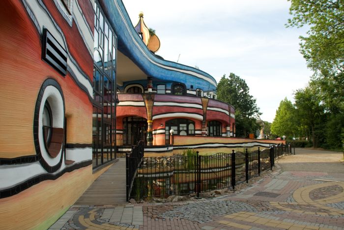 Ronald McDonald Kindervallei in Valkenburg met golvende blauw-rode gevel, loopbrug en vijver met hekwerk aan de voorzijde.