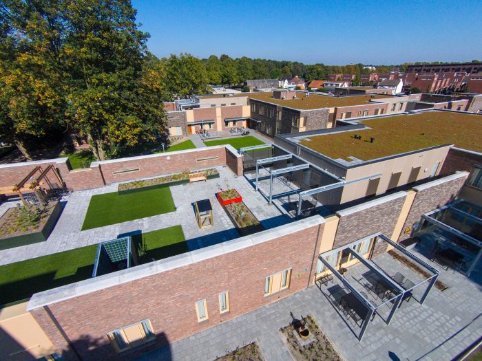 Hof verpleeghuis Venray, sierbestrating met grasvakken, zitbanken en baksteengevels.