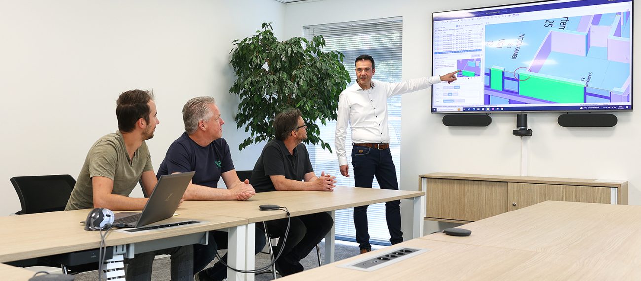 Presentatie van een BIM-model op groot scherm tijdens overleg, waarbij een medewerker het ontwerp toelicht aan drie collega’s.