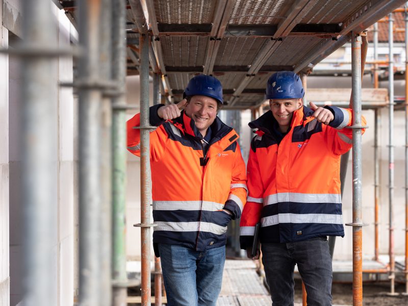 Twee medewerkers in bouwkleding geven een duim omhoog op een bouwplaats