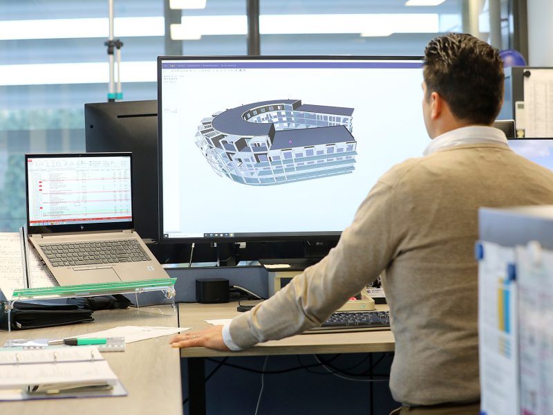 Medewerker werkt aan 3D-gebouwmodel in BIM-software op groot scherm in moderne kantooromgeving.