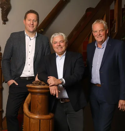 Drie mannen in pakken staan bij houten trapleuning in interieur