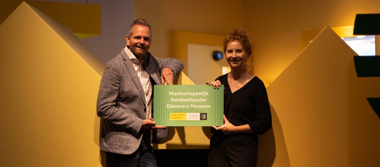 Twee mensen poseren met een bord waarop staat "Maatschappelijk Aandeelhouder Discovery Mseum"
