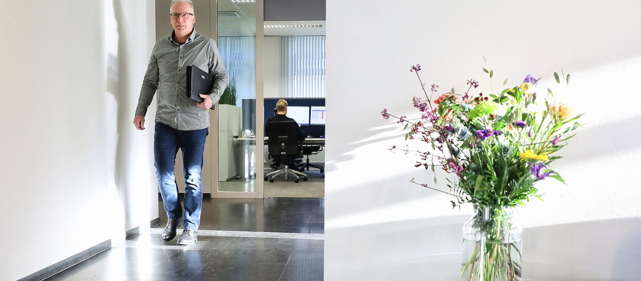 Medewerker loopt door licht kantoor met glazen werkruimte op achtergrond en veldboeket op tafel