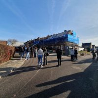Groep mensen loopt op straat met op de achtergrond een rij woningen in de steigers
