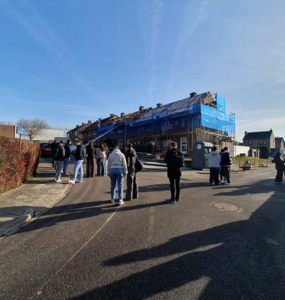 Groep mensen loopt op straat met op de achtergrond een rij woningen in de steigers