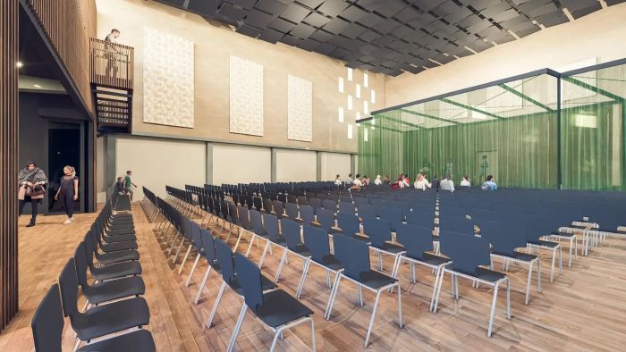 Impressie van multifunctionele zaal met stoelenopstelling, bezoekers en podiumzone achter groene afscheiding.