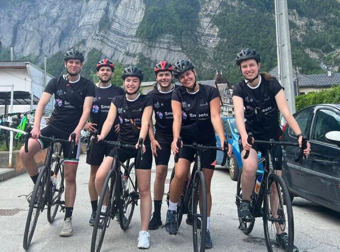 Een team van fietsers poseert met op de achtergrond de Alpen