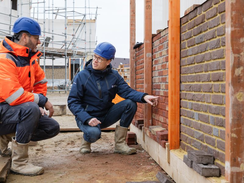 Twee collega's staan naast een gemetselde muur