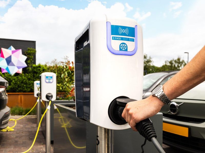 Elektrische auto wordt aangesloten op laadpaal naast geparkeerde voertuigen