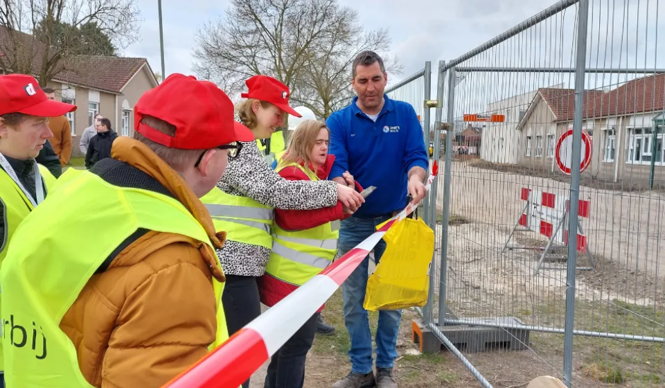 Groep met veiligheidshesjes knipt lint door bij afgezette bouwplaats met woningen