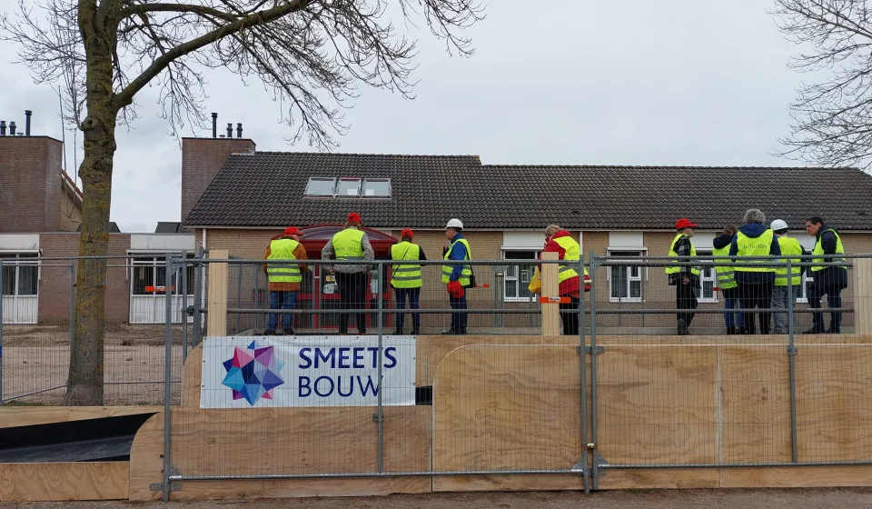 Groep met veiligheidshesjes op afgezette bouwplaats voor gebouw van Smets Bouw