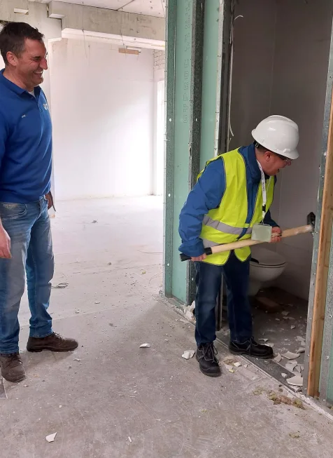 Persoon met veiligheidshelm en hamer tijdens werkzaamheden in onafgewerkte binnenruimte