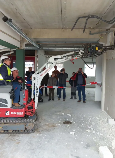 Sloopwerk in binnenruimte met minigraver en omstanders achter afzetlint