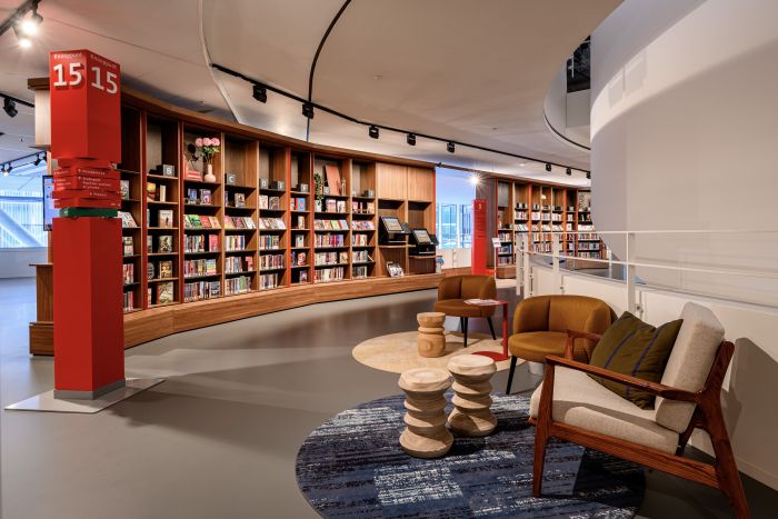 Gezellige leesplek met designfauteuils, stapelbare houten krukjes en rond kleed naast de balustrade.