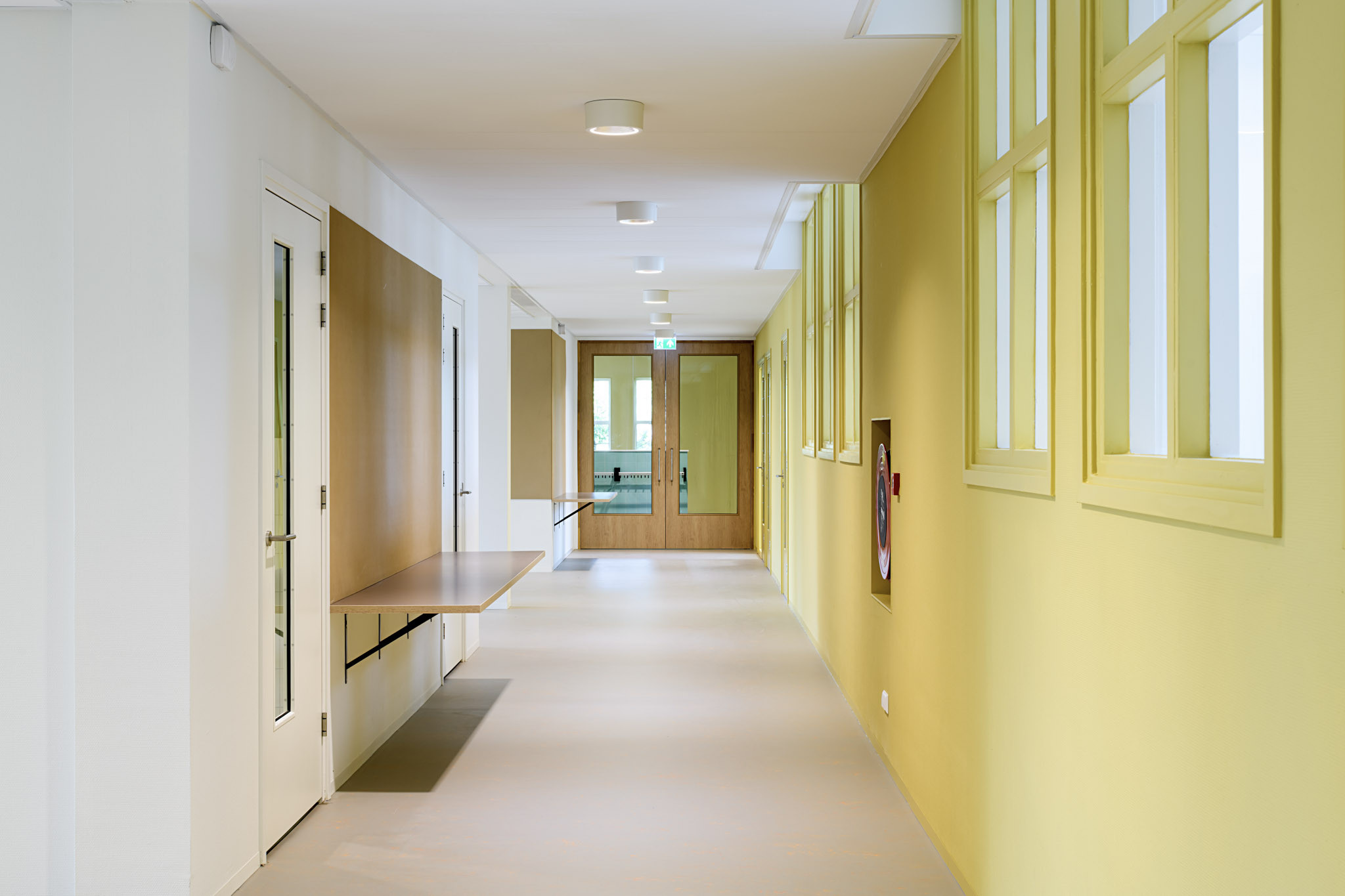 Schoolinterieur De Fakkel Utrecht: brede corridor met gele kasten, witte deuren en kapstokwand