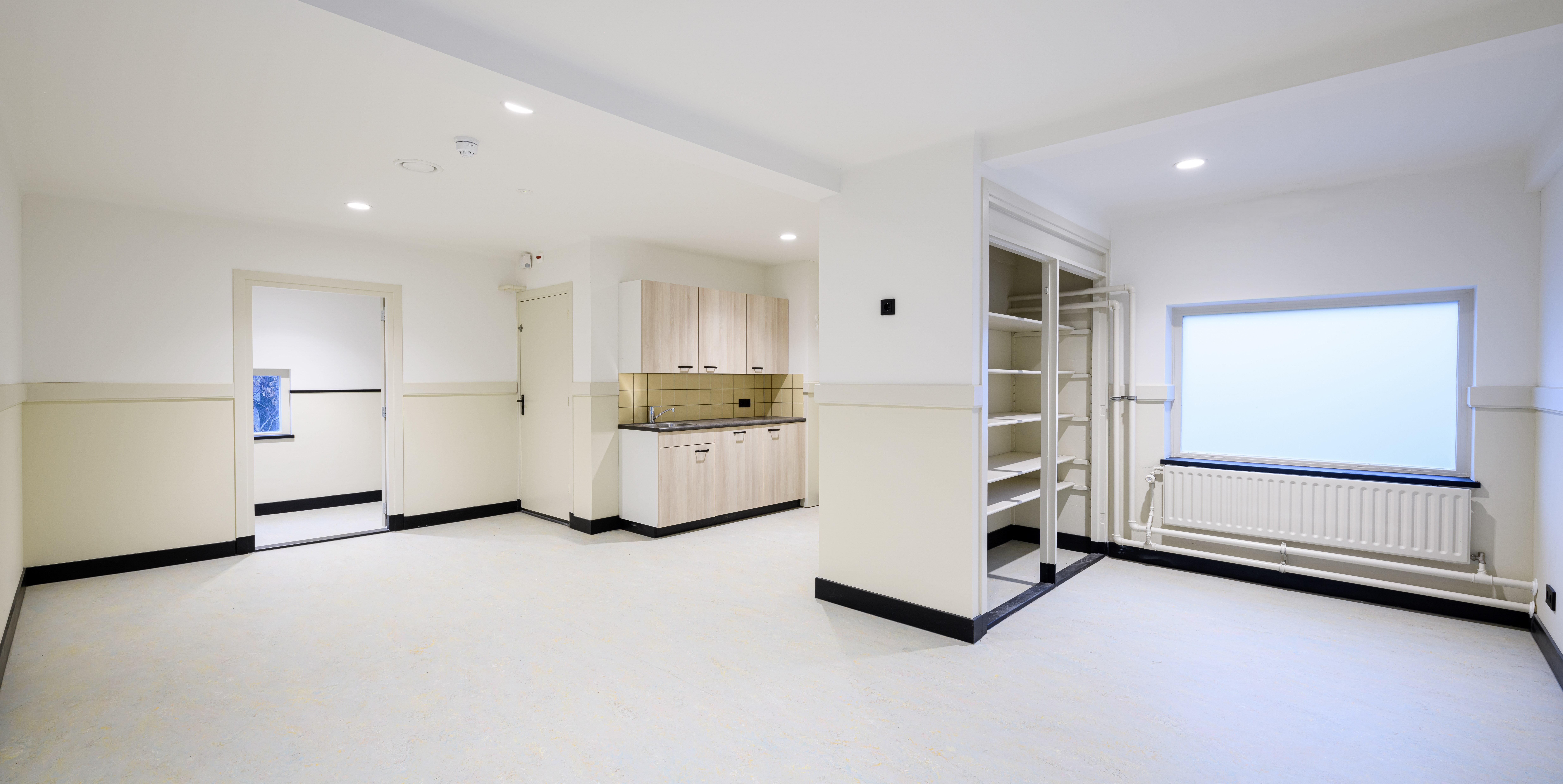 Heldere klas/atelier: crèmekleurige lambrisering, zwarte plinten, lichte vloer en pantry.