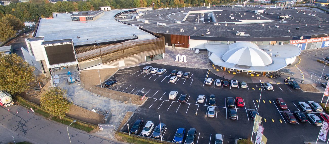 Luchtfoto van een groot winkelcentrum met parkeerplaats en omliggende gebouwen.
