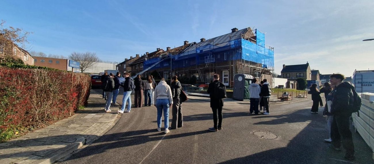 Groep mensen loopt op straat met op de achtergrond een rij woningen in de steigers