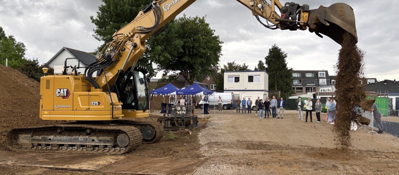 Graafmachine schept aarde op een bouwterrein terwijl mensen toekijken.