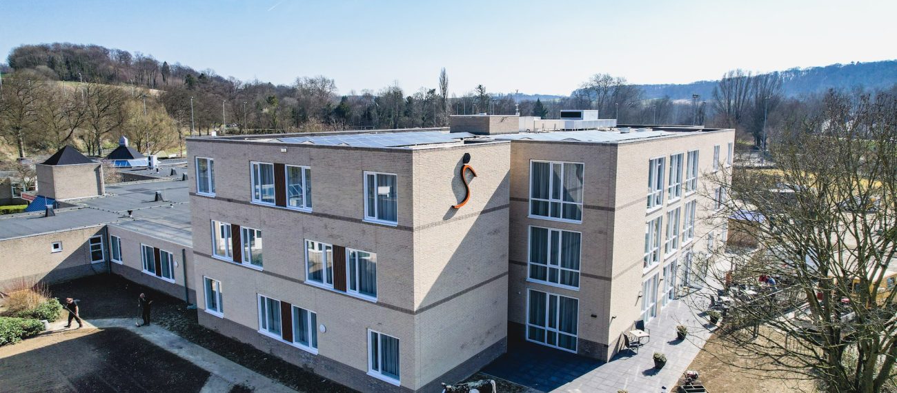 Modern gebouw met meerdere verdiepingen, grote ramen en een fiets bij de ingang, omgeven door bomen.