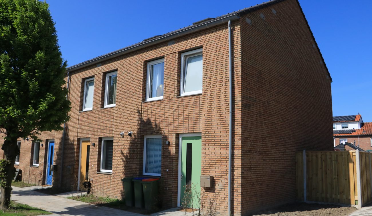 Conceptwoningen Klundert: hoek rijwoning baksteen met groene deur, nieuwe stoep en voortuin, zonnig.