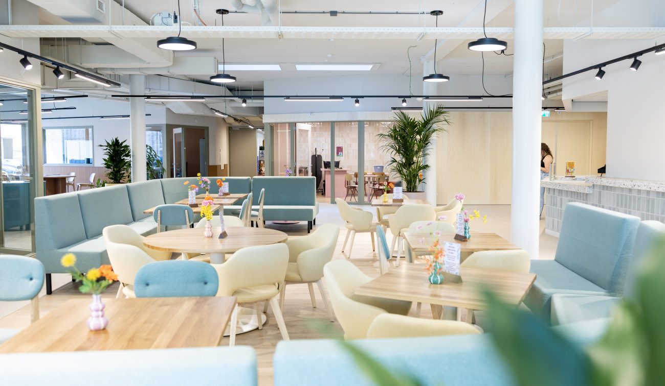 Lichte ontmoetingsruimte met ronde tafels, pastelkleurige stoelen en planten.