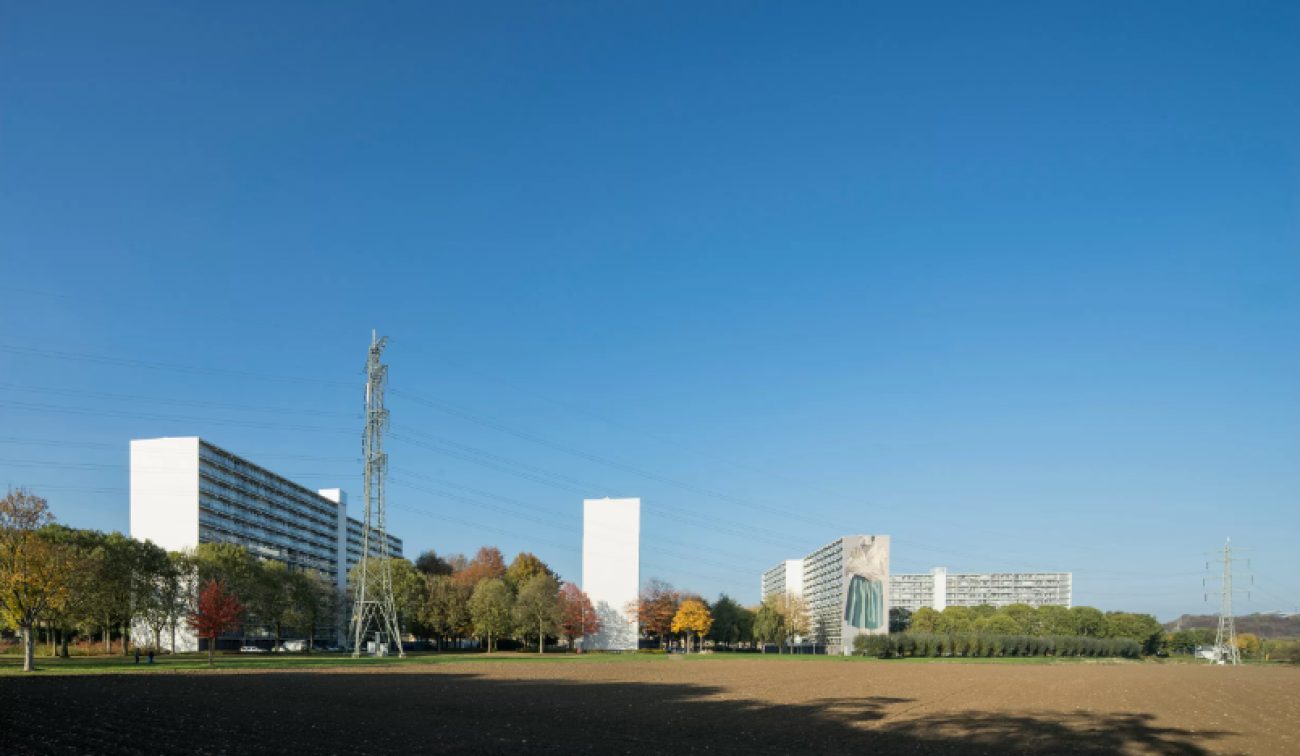Panorama Heerlerbaan Heerlen met gerenoveerde galerijflats en kunstgevel, gezien over veld.