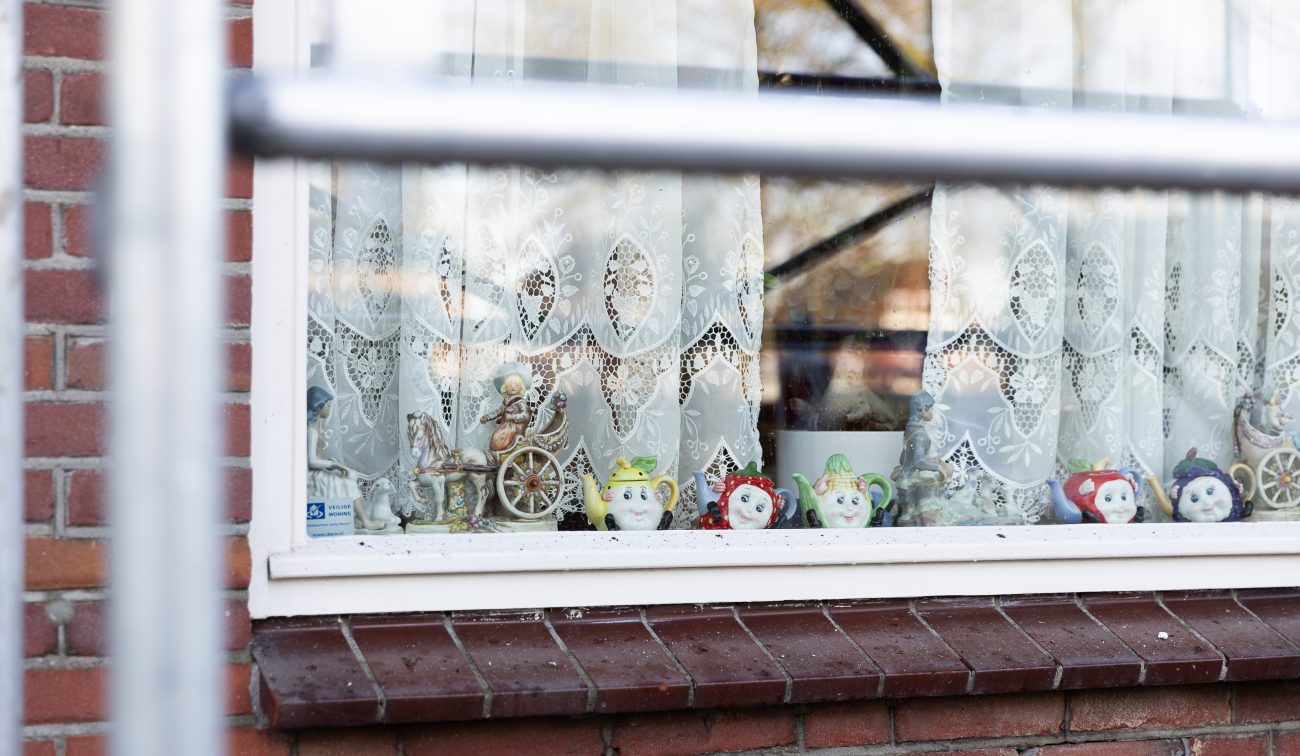 Detailfoto van een raam in de wijk Tuinzigt Haagpoort met porseleinen beeldjes voor het gordijn, vastgelegd tijdens het groot onderhoudsproject.