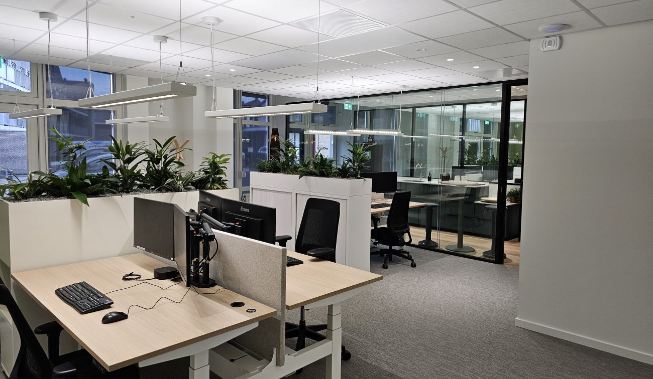 Moderne kantoorruimte met zit-sta bureaus, computerschermen en bureaustoelen.