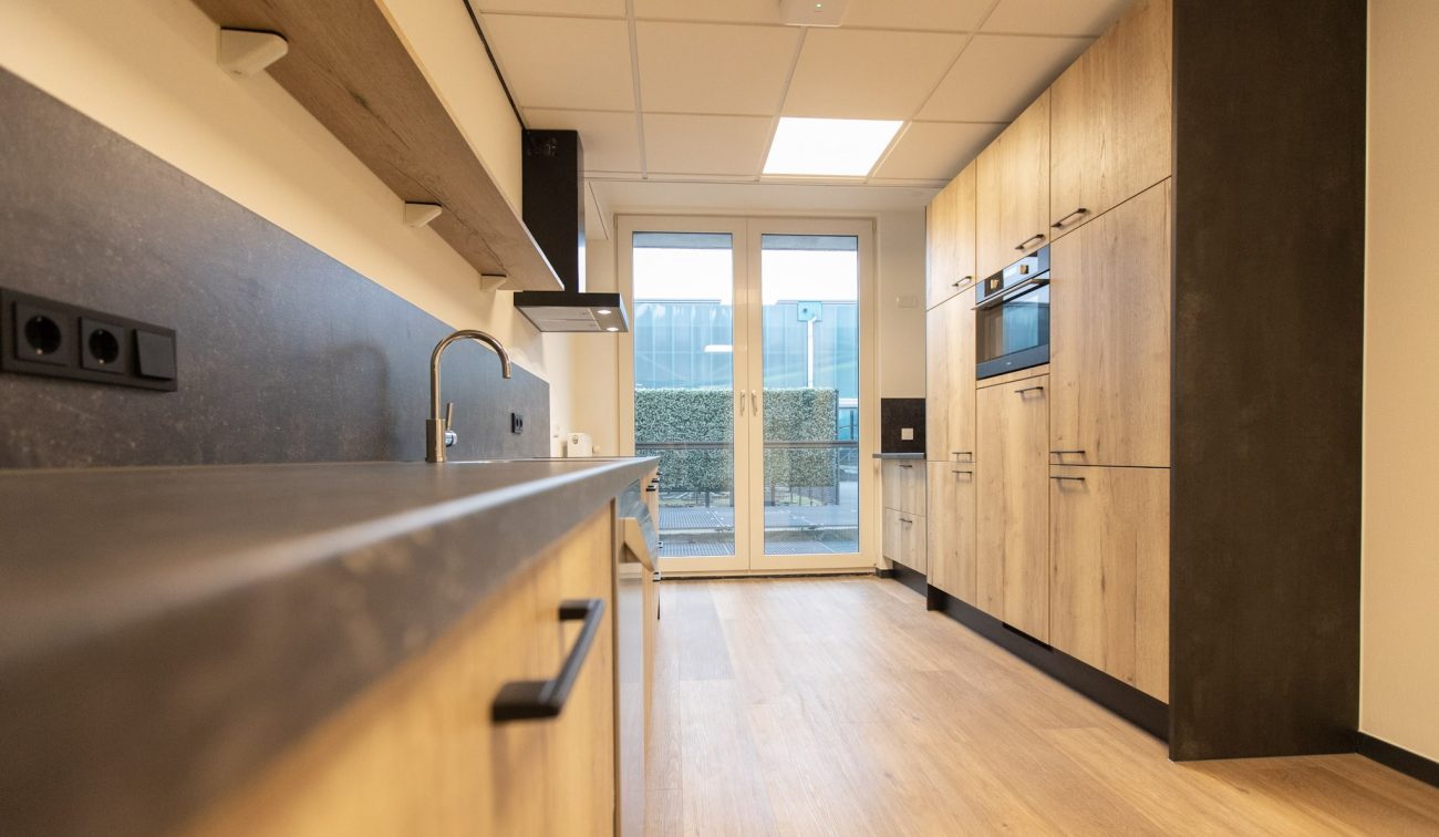 Moderne keuken met houtlook kasten, donker werkblad en dubbele deur naar patio.