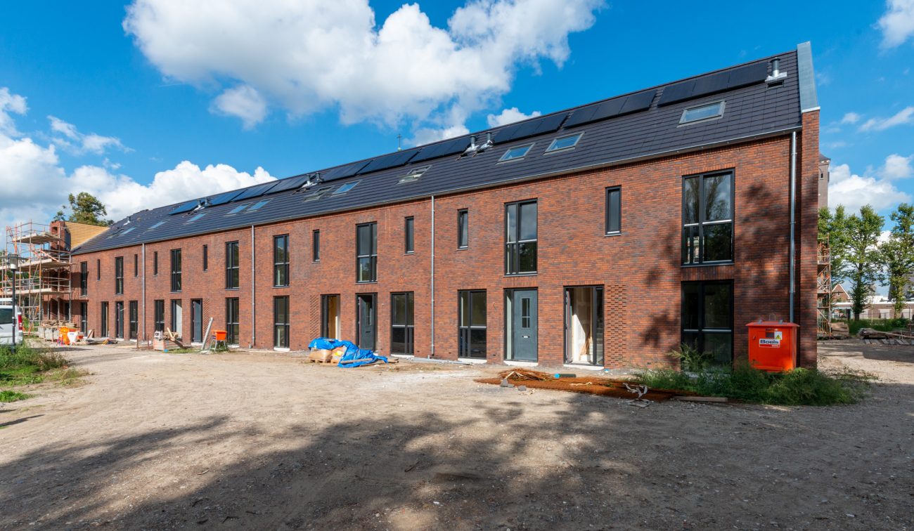 Kloostervelden Sterksel – rijwoningen in rood baksteen met donkere pannendaken en zonnepanelen, bouwplaats met zandbaan en materialen
