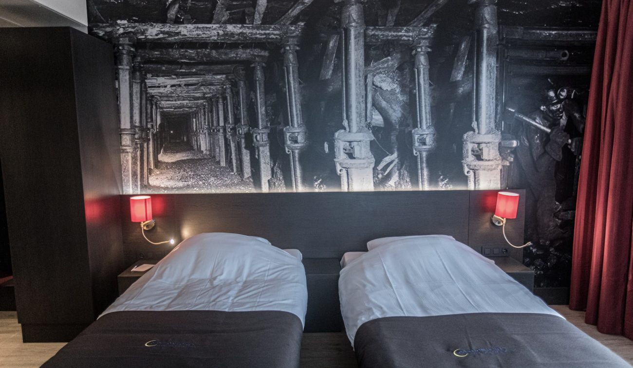 Interieur hotelkamer Geleen – twinbed opstelling met industriële muurprint en rode lampen