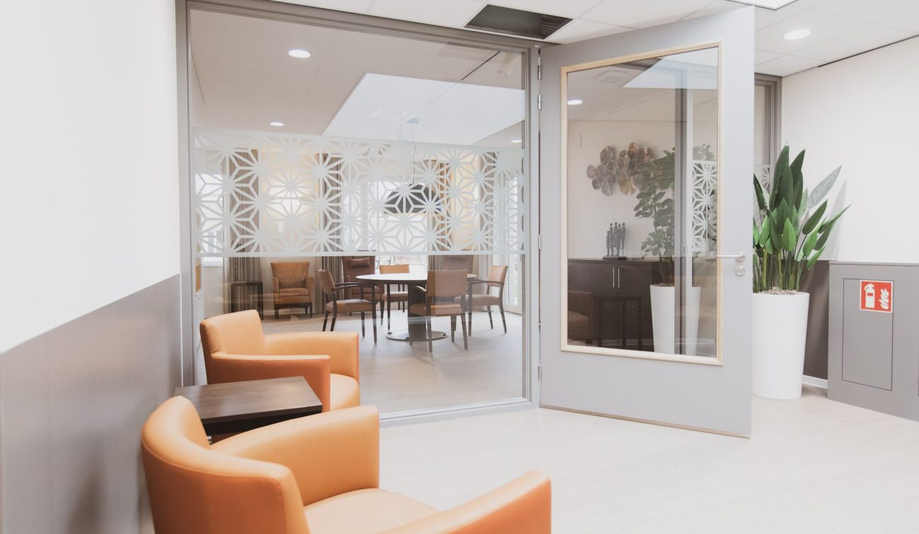 Interieur verpleeghuis Panhuys Hulsberg met oranje loungefauteuils en glazen scheidingswand.
