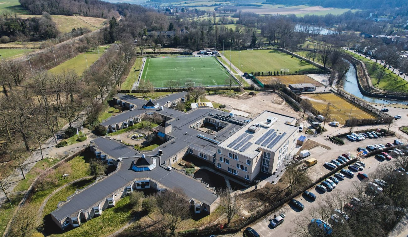 Luchtfoto zorgcomplex Valkenheim Valkenburg met zonnepanelen en omliggende sportvelden.”