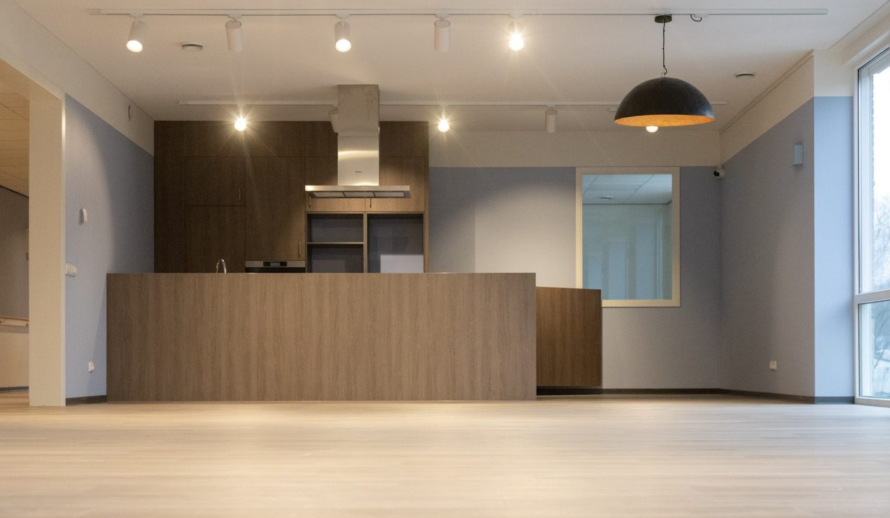 Interieur zorgcomplex Valkenburg: moderne keukenwand met kookeiland en grote hanglamp.