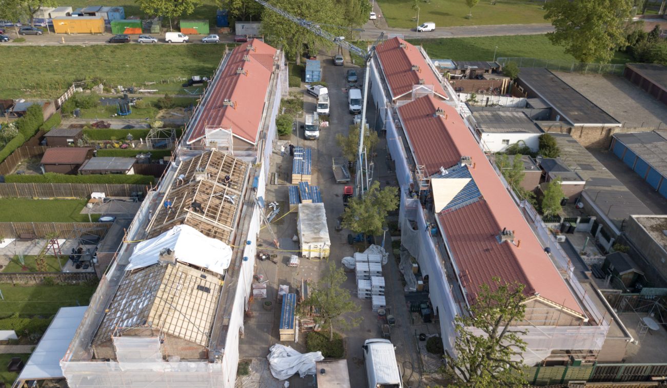 Luchtfoto renovatie Heilust Kerkrade: rijwoningen in steigers met nieuwe rode dakpannen.