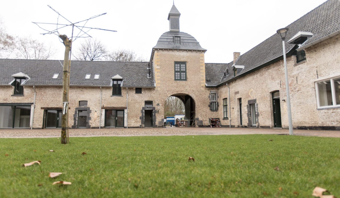 Binnenplaats carréhoeve met poortgebouw en klokdak, gezien over een groen gazon — herbestemming tot appartementen, Maastricht.
