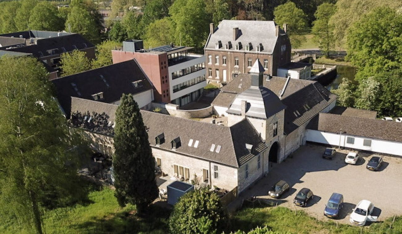 Luchtfoto van historische carréhoeve met poortgebouw en binnenplaats, naast moderne appartementen — herbestemming tot woningen in Maastricht.