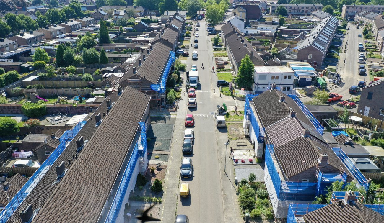 Luchtperspectief straat met aaneengesloten woningen in onderhoud, werkbusjes en hekken — Groot onderhoud 154 woningen Nieuwdorp Stein