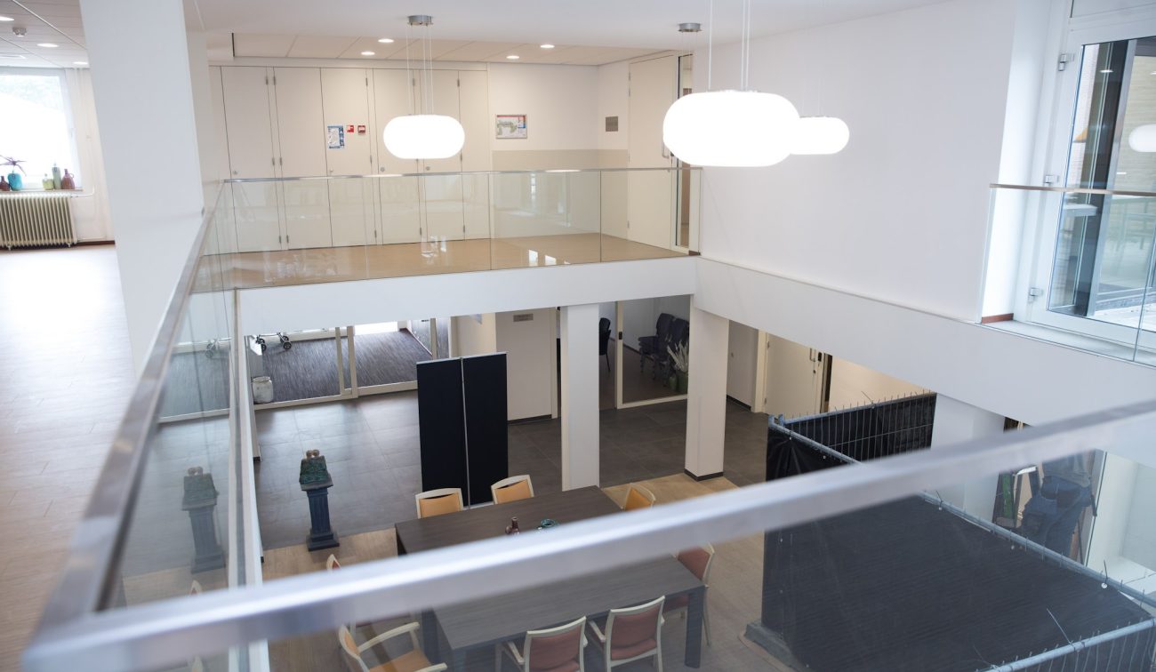 Interieur Beukeloord: open vide met glazen balustrade en grote hanglampen.