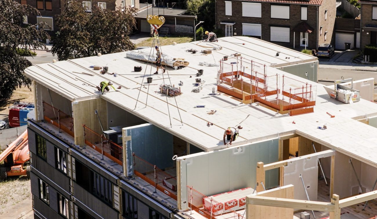 Appartementengebouw in aanbouw met prefab verdiepingsvloer en monteurs tijdens montagewerkzaamheden op het dak