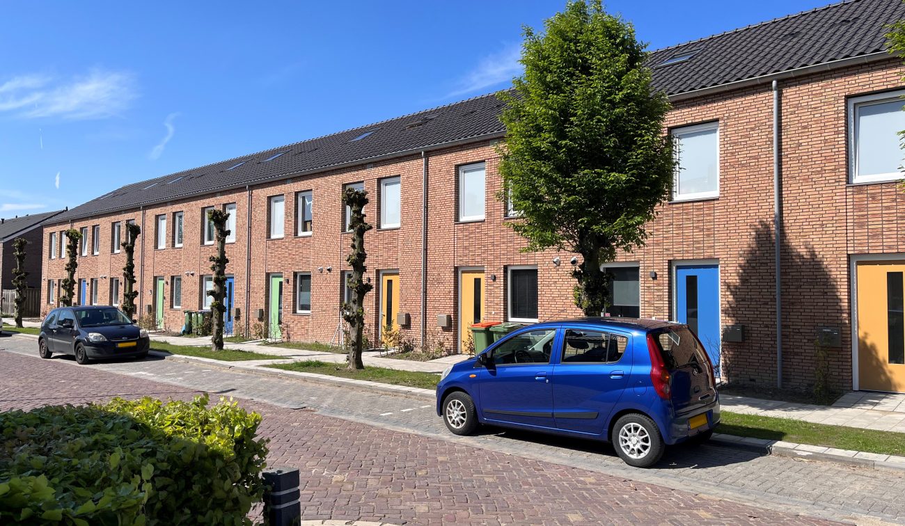 Conceptwoningen Klundert: rijhuizen baksteen met kleurige deuren, gesnoeide bomen en autos, zon