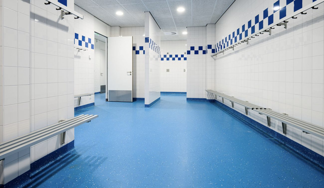 Hoge, lichte sportruimte met nieuwe sportvloer en belijning, akoestisch lamellenplafond, klimvoorzieningen (ringen/rek) en wandbescherming met grafische prints.